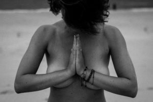 kobieta medytuje na plaży, ręce w mudrze modlitewnej